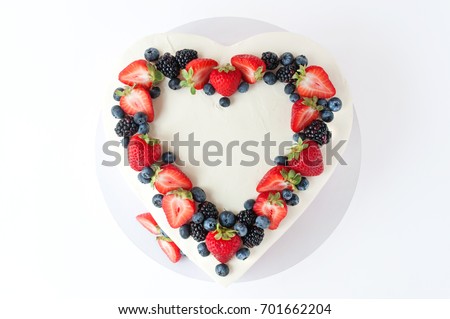 Valentine cake in form of heart with whipped pink cream, decorated with strawberries, blueberries and blackberry on white background. Picture for a menu or a confectionery catalog. Top view.