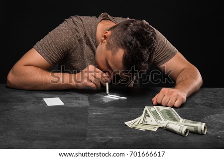A young junkie with money on a black background. A drug addict with cash sitting at the table. Copy space. Royalty-Free Stock Photo #701666617