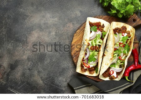 Mexican tacos with pulled beef,fresh cucumber and yogurt dressing on a cutting board over dark slate,stone or metal background.Top view with copy space.