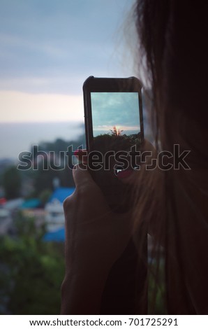 A young woman photographs the sunset at the seaside. Grainy photo.