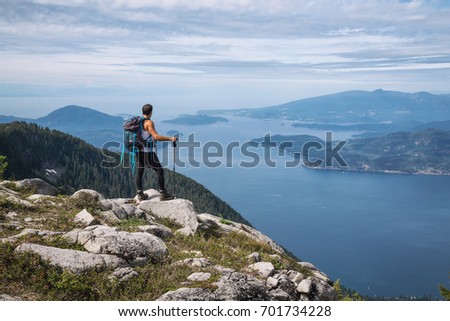 Latin American Male Hiker is standing on top of the rocky peak overlooking the beautiful landscape. Picture taken on the way up to The Lions Mountain, North of Vancouver, British Columbia, Canada.