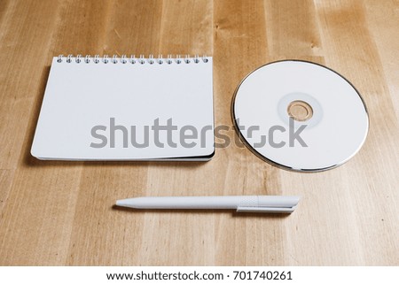 mock up of blank printable compact cd or dvd disc, pen and white notebook on wooden office table