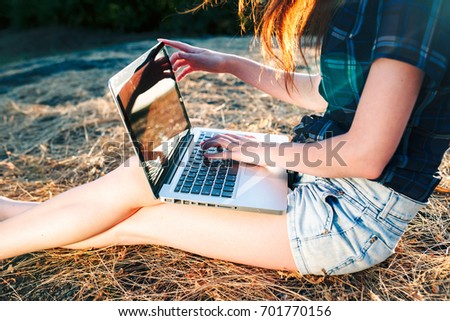 Happy casual beautiful woman watching videos or enjoying entertainment content in a laptop sitting in a straw field outdoors in a sunny day