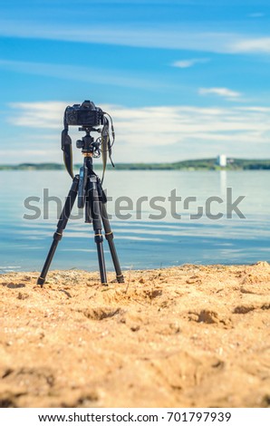 A camera on a tripod on the sandy seashore removes the seascape. Photographic equipment in the process of shooting the landscape. Camera while taking a photo or time-lapse