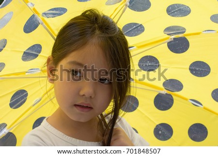 portrait of little girl holding yellow umbrella under showering rain