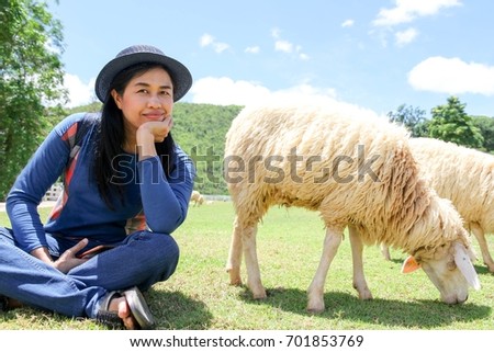 Asian woman relax in sheep farm , she sitting on green grass and feels so happy 