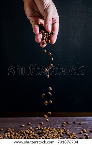 Coffee beans are falling from the black background hands.