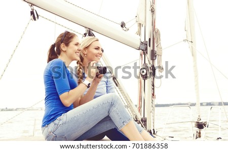 Two beautiful, attractive young girls with camera taking pictures on yacht and enjoying a day. Summertime, vacation concept.