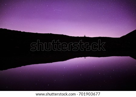 Small Man in silhouette in the mountains at beautiful night sky with stars and Milky Way reflected in the lake