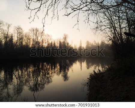 The calm river with mirror like reflection and mystic fog at the sunset