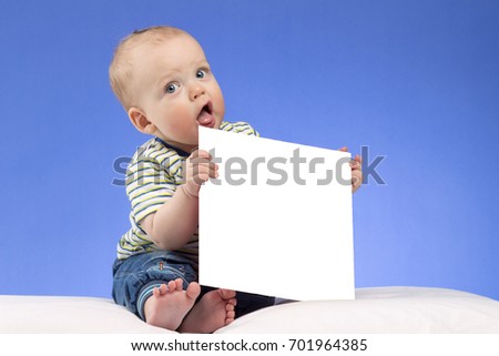 Funnt infant kid with white piece of paper on the blue background. Cute toddler with mock-up. Stufio shot with copy space.