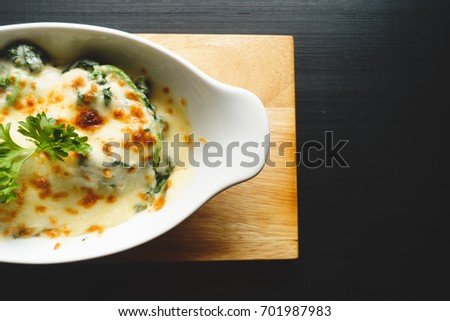 Spinach lasagna or Baked Spinach with Cheese in white bowl on black wooden table, toned picture