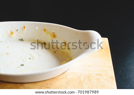 Empty white bowl after meal with food stains on the bowl on black wooden table, toned picture