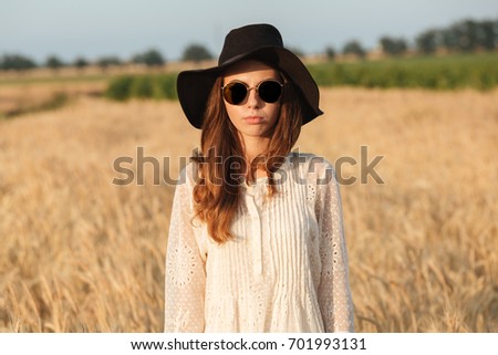 Picture of amazing young woman wearing sunglasses standing in the field. Looking camera.