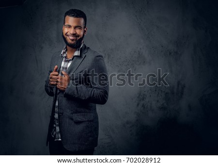 Studio portrait of Black hipster male dressed in a fleece shirt and a jacket posing over grey artistic background.
