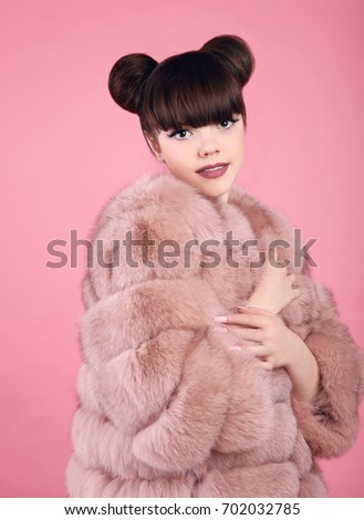 Beauty makeup. Fashion teen girl model in fur coat. Brunette with matte lips and bun hairstyle posing over studio pink background.