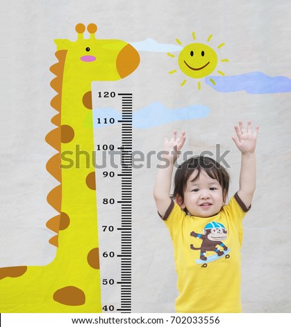 Closeup happy asian kid stand for measure height with cute cartoon at the marble stone wall textured background in growth of kid concept