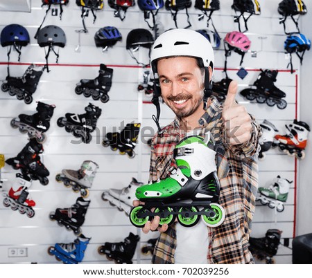 Smiling pleasant  guy deciding on new roller-skates in sports store 