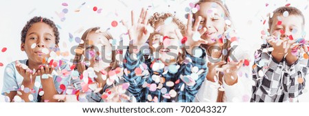 Group of smiling children in casual clothes throwing confetti around them