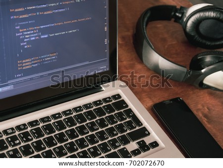 Php code on laptop's display with cellphone and earphones on working place