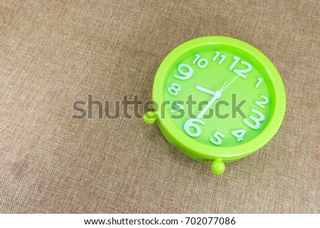 Green alarm clock on brown sackcloth background show half eight o'clock or 8:30 a.m.