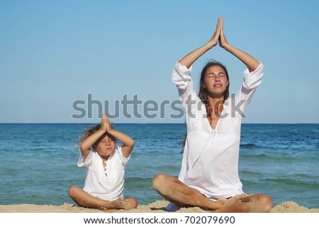 Mother and daughter are engaged in yoga at sea, in white clothes are smiling, the background of sea blue water.