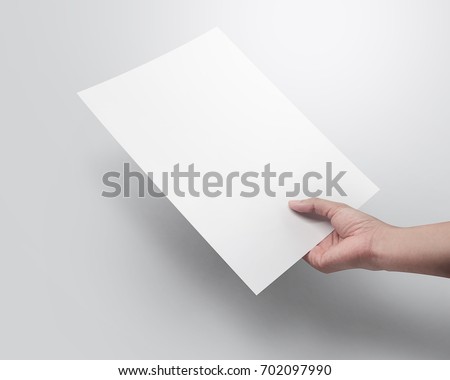 Right hand holding blank paper sheet A4 size or letter paper on grey background. Royalty-Free Stock Photo #702097990