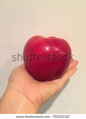 A hand of an Asian woman holding a red apple with a white background.