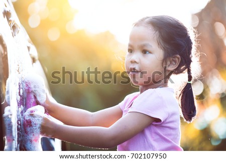Happy asian child girl having fun to help parent washing car  with sunlight