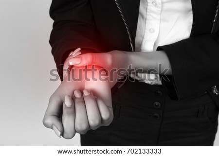 Young businesswoman  holding sore wrist in her hand over gray background. Black and white with red accent. Pain concept close-up