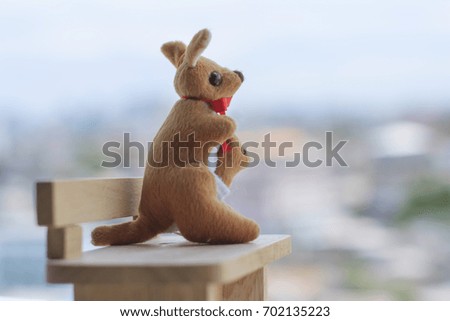 Kangaroo mother and baby doll sitting on mini wood bench look at the city view, feeling lonely. Kangaroo toy famous Australian souvenir for tourist.