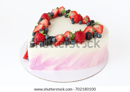 Valentine cake in form of heart with whipped pink cream, decorated with strawberries, blueberries and blackberry on white background. Picture for a menu or a confectionery catalog.