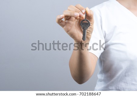 Woman hand giving keys on grey background
