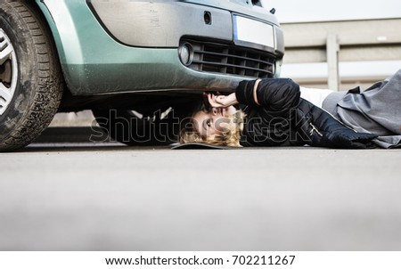 Auto assistance and insurance, troubles while traveling concept. Woman trying to repair her broken car, checking what is under automobile.