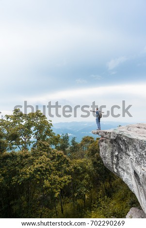 Male solo adventure traveler standing on a cliff with open arms with the rain forest and jungle below.