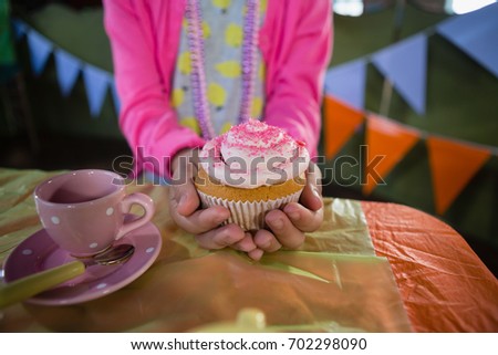 Mid-section of birthday girl holding a cupcake at home