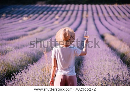 Young woman drink rose wine in the sunset lavender field, standing back to the camera, Provence, south France Royalty-Free Stock Photo #702365272