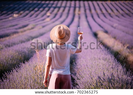Young woman drink rose wine in the sunset lavender field, standing back to the camera, Provence, south France Royalty-Free Stock Photo #702365275
