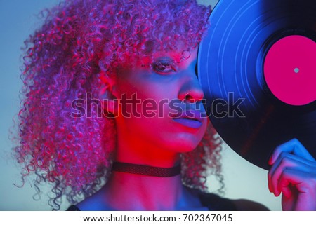 portrait of a disco woman holding a retro vinyl with eighties music and neon light Royalty-Free Stock Photo #702367045