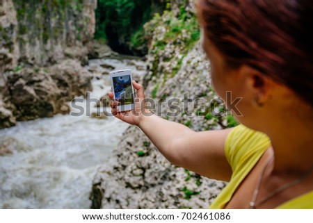 Girl traveler takes a photo of a lush mountain river in a ravine on a smartphone, selective focus