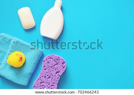 Bath products flat lay. Organic baby soap, white shampoo bottle, towel, purple sponge and yellow rubber duck on a blue background. Top view photography
