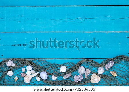 Seashells with fish net border on antique rustic teal blue wood background; blank beach sign with painted wooden copy space