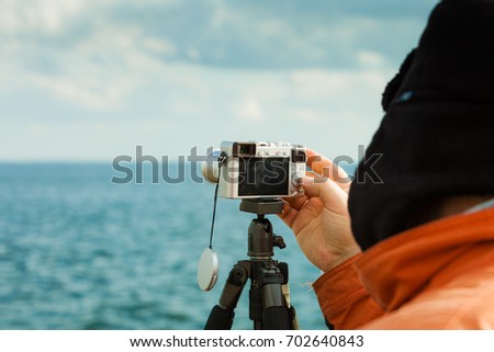Man having leisure time walking on coastline during autumnal weather taking pictures using camera