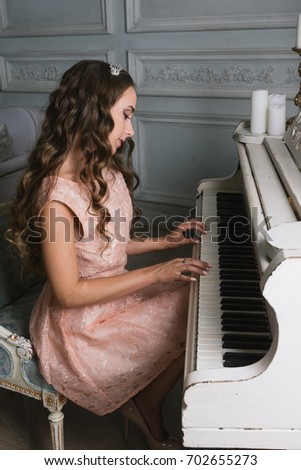 Pretty woman playing grand piano. Beautiful young lady in a pink lacy dress, in a vintage luxury grey interior. long curly hair, fashion makeup
