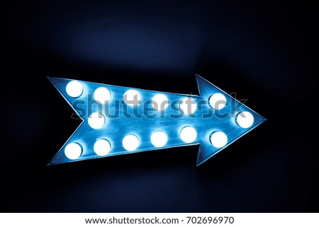 Blue vintage bright and colorful illuminated display arrow sign with light bulbs against a blue dark background