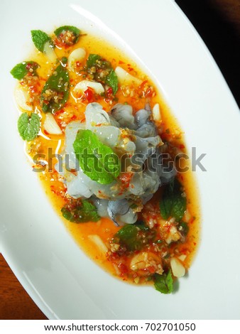 The picture of spicy raw shrimp salad on white dish above  wooden table.