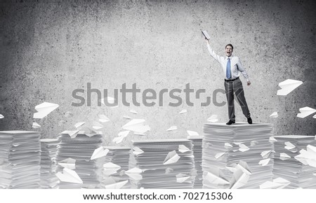 Businessman keeping hand with book up while standing flying paper planes with grey background. Mixed media.