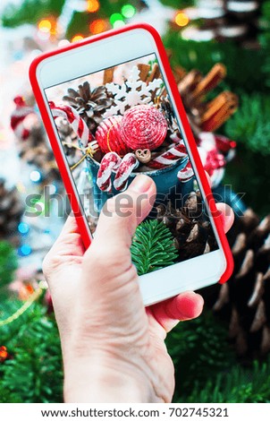 Holiday Christmas Composition with Hand Holding Phone Shooting Photo Fir Tree Toys Gifts Red Ball Candy Cane Pine Cones Snowflakes Cinnamon Festive Background