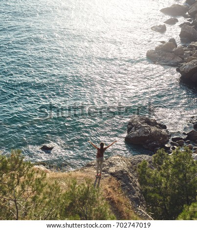 Back view of woman standing on the sea coast Between pines and Enjoying the sunset