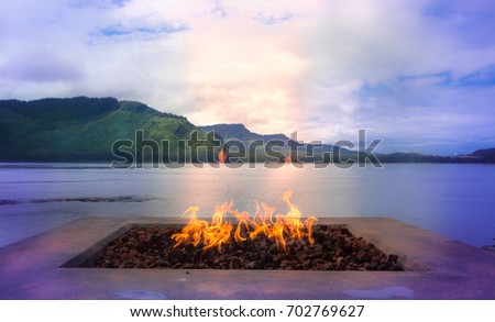 A wood fire on a marble base placed outdoors with a sea and mountains as a background.